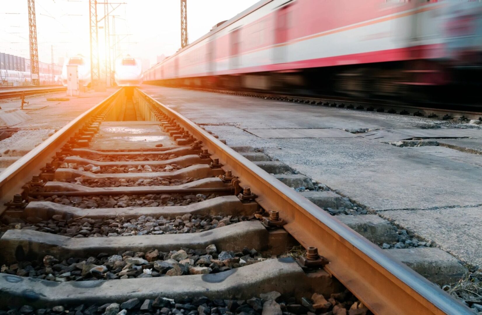 A train is traveling down the tracks in front of the sun.